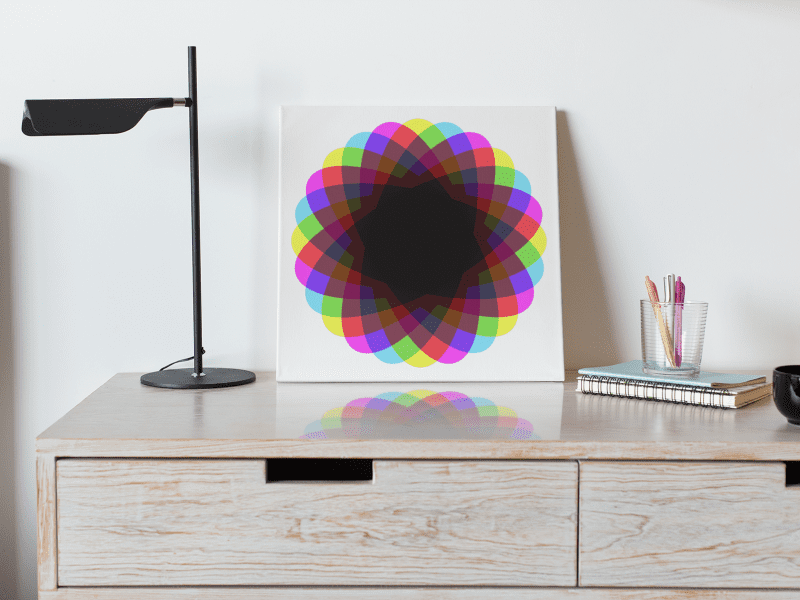 Abstract star artwork in vivid cyan, magenta and yellow and black. Printed on art board. Set on top of a chest of drawers alongside a desk lap, notebooks, pens and a coffee cup.
